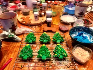 Decorated Christmas tree cookies with green icing and colorful sprinkles on a wire cooling rack with baking ingredients in the background from Annual Poppy Kids Pediatric Dentistry Cookie day.